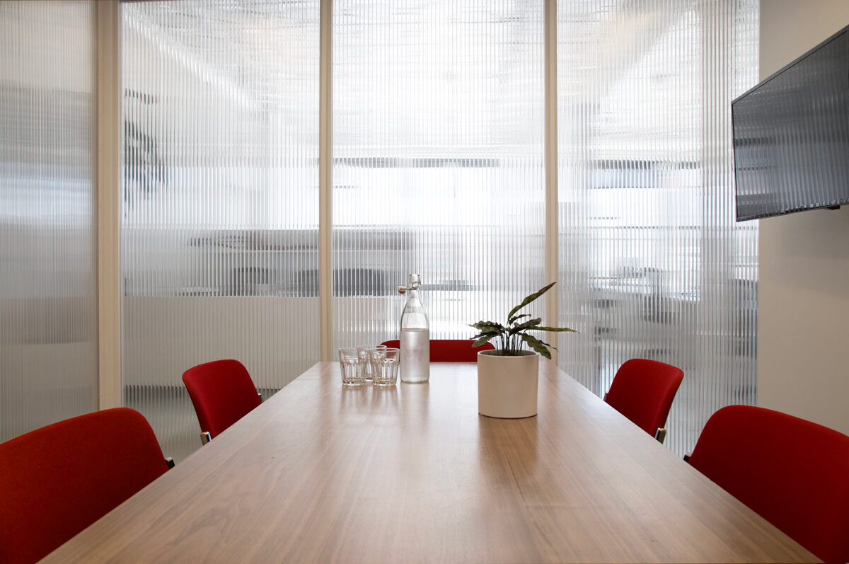 Small meeting room with red chairs, a wooden table, and reeded glass walls