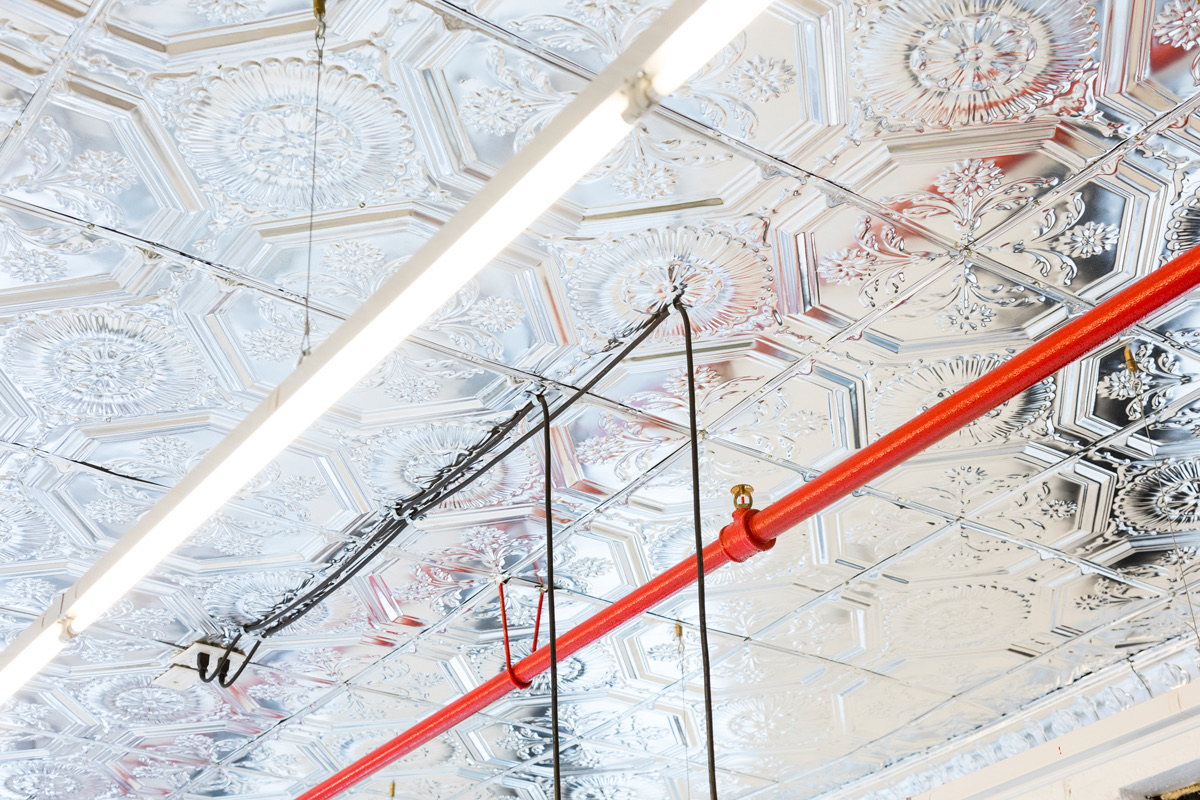 Pressed tin-tile ceiling of the loft with a fluorescent tube and a painted red sprinkler pipe running across it