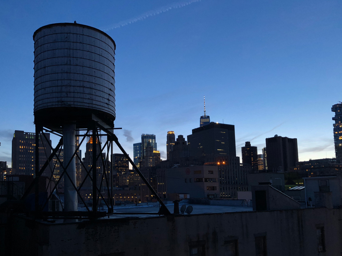 View from the Based In rooftop at dusk: a wooden water tower against the Lower Manhattan skyline