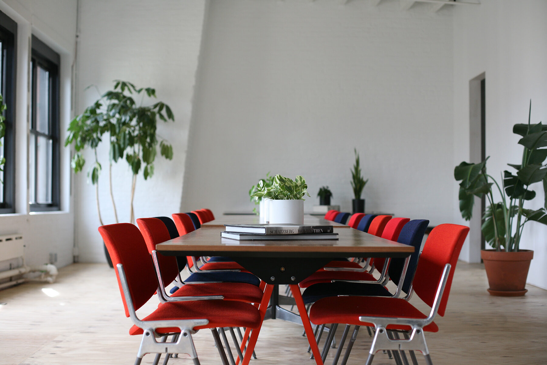 Conference table ringed with red and navy chairs in a bright white-brick room