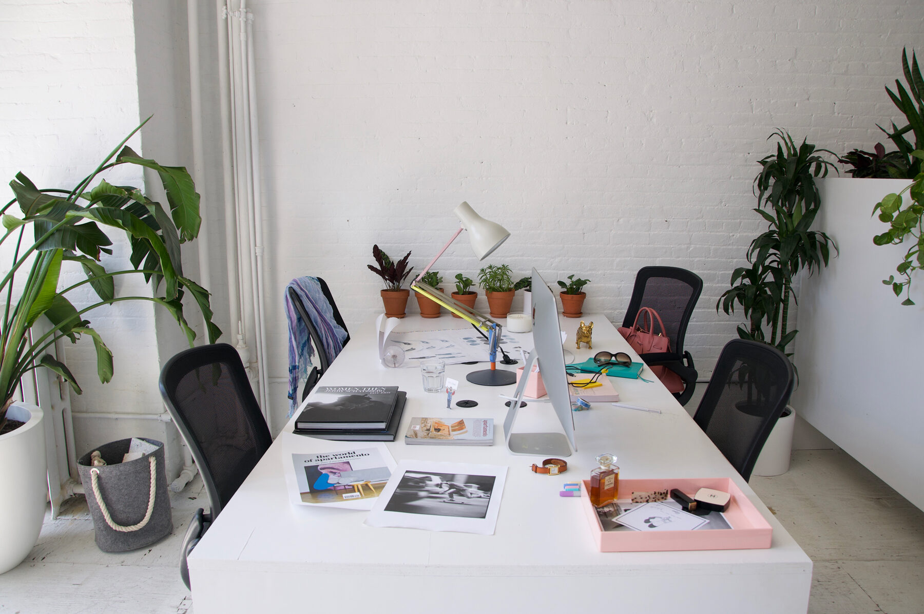 White work table styled with books, a lamp, plants, and black task chairs